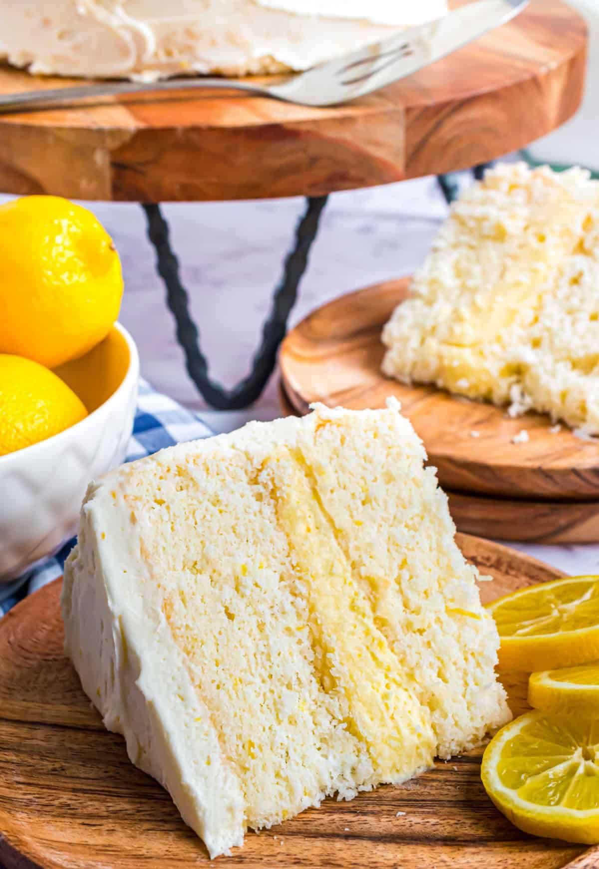 Slice of lemon layer cake with lemon curd filling on a wooden plate.