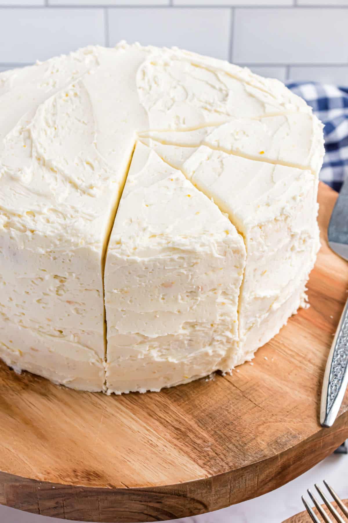 Lemon layer cake on a wooden cake plate with several slices cut.