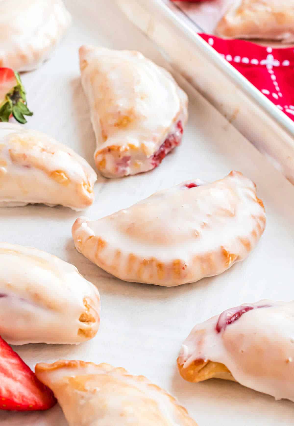 Glazed strawberry filled hand pies on a parchment paper lined cookie sheet.