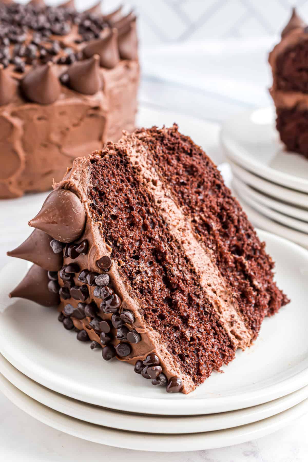 Slice of chocolate cake on a stack of white plates.