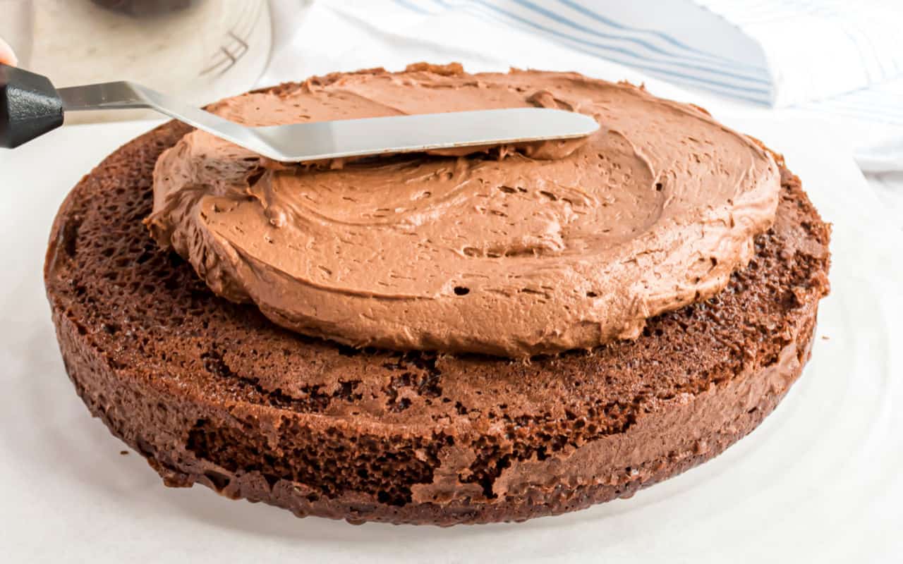 Chocolate ganache frosting being spread over a chocolate cake.