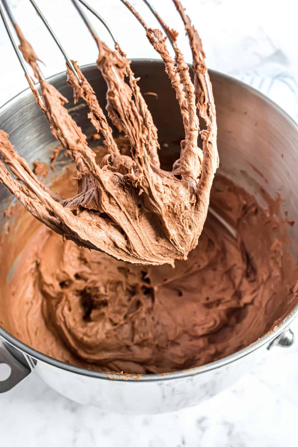 Chocolate frosting in a mixing bowl with whisk attachment.