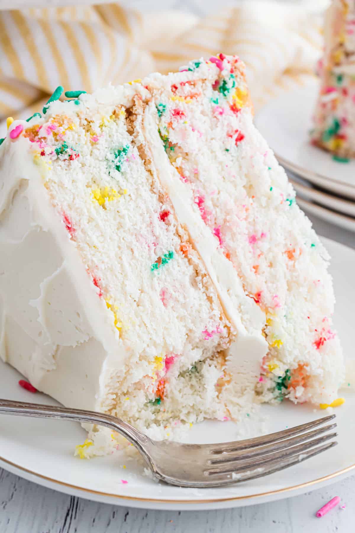 Slice of funfetti layer cake with vanilla frosting on white plate.