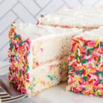 Funfetti layer cake covered in vanilla frosting and sprinkles on the sides.