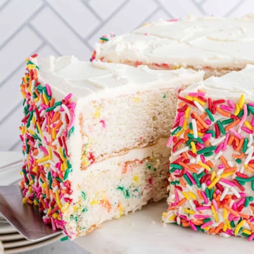 Funfetti layer cake covered in vanilla frosting and sprinkles on the sides.