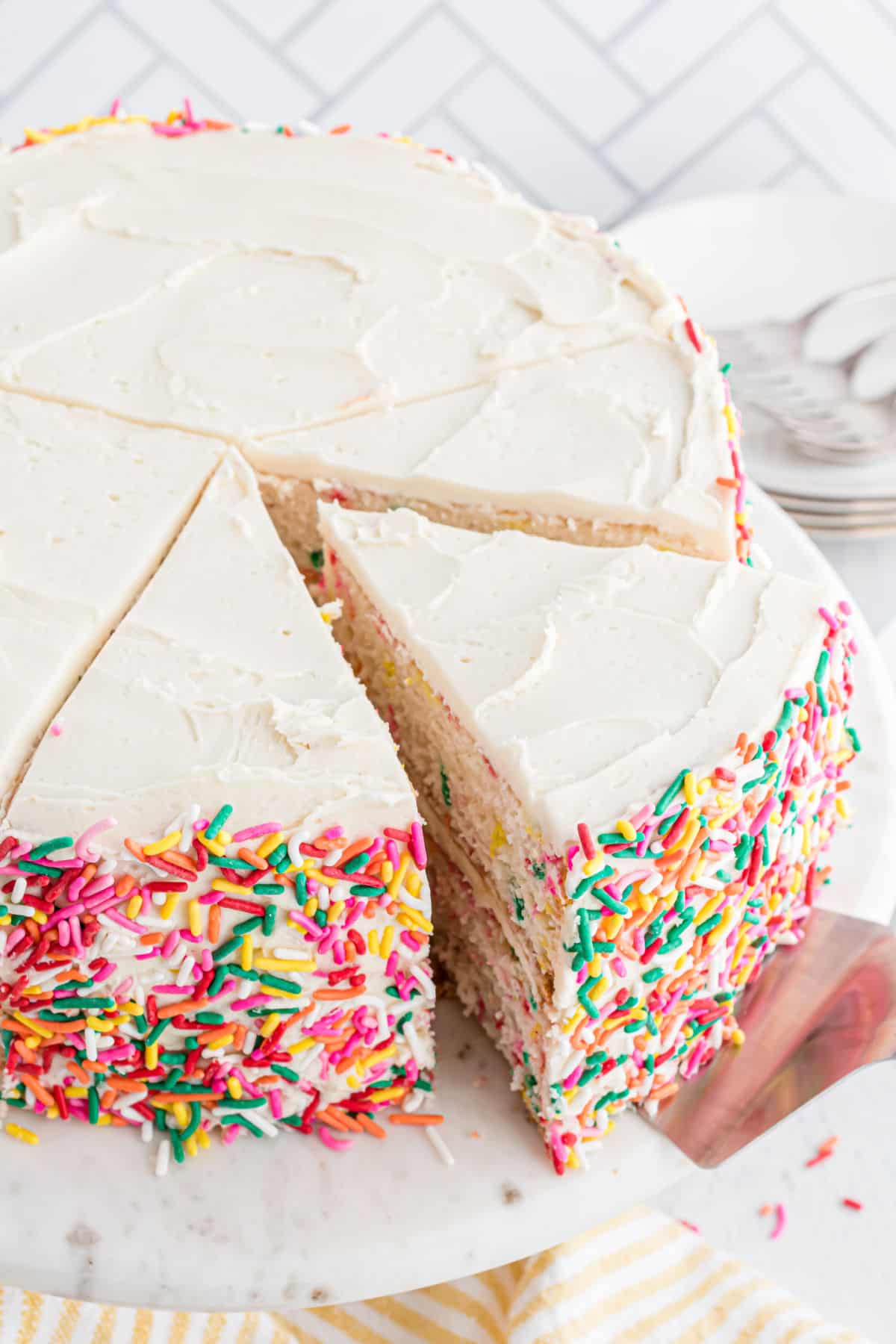 Funfetti layer cake with vanilla frosting and a gash being remnoved.  Vanilla Funfetti Cake funfetti cake sliced