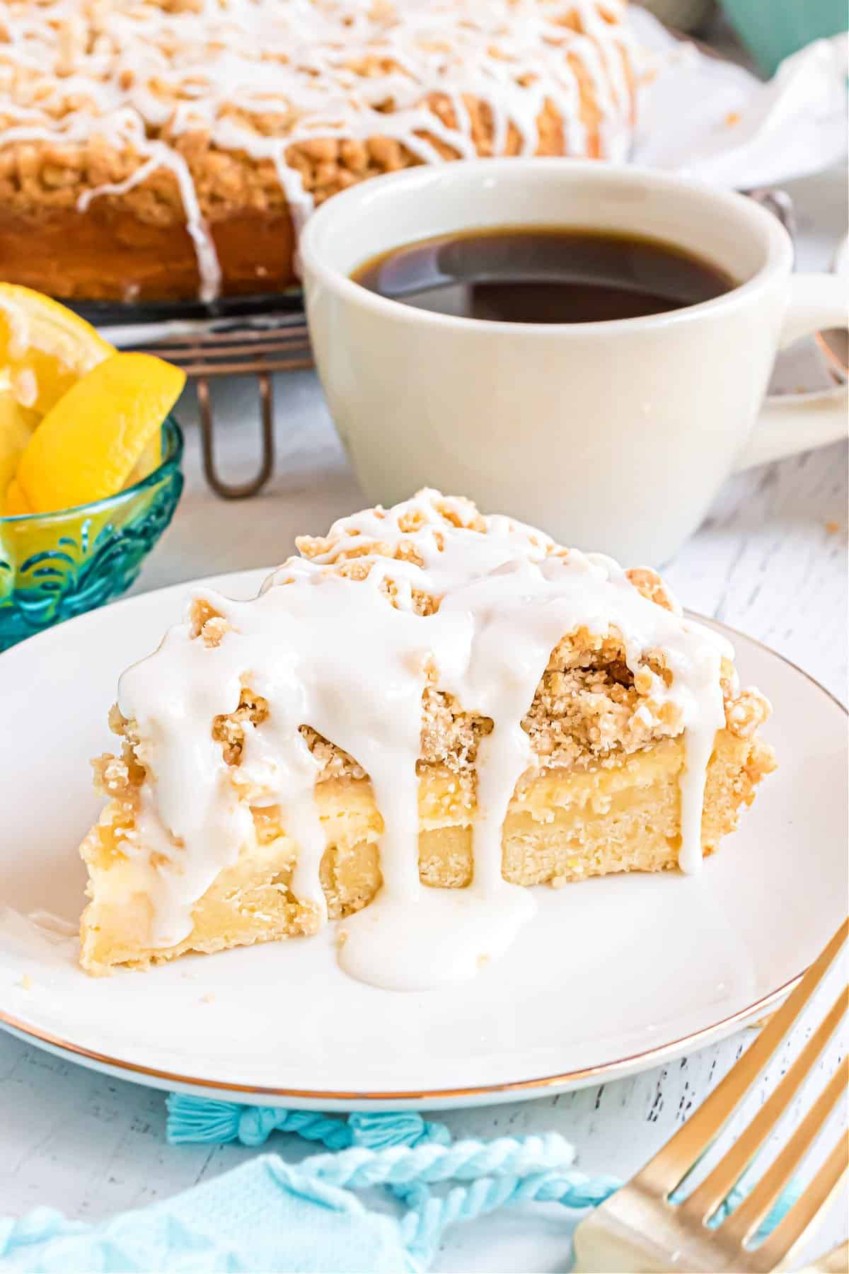 Slice of lemon crumb coffee cake on a plate with mug of coffee.