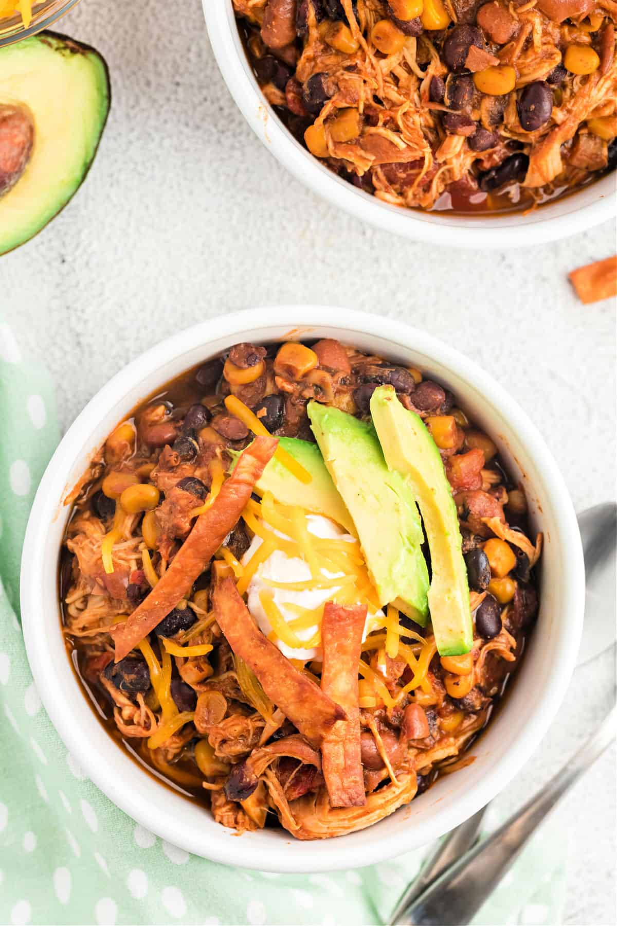 Chicken chili in a white bowl topped with sour cream, cheese, and avocado.