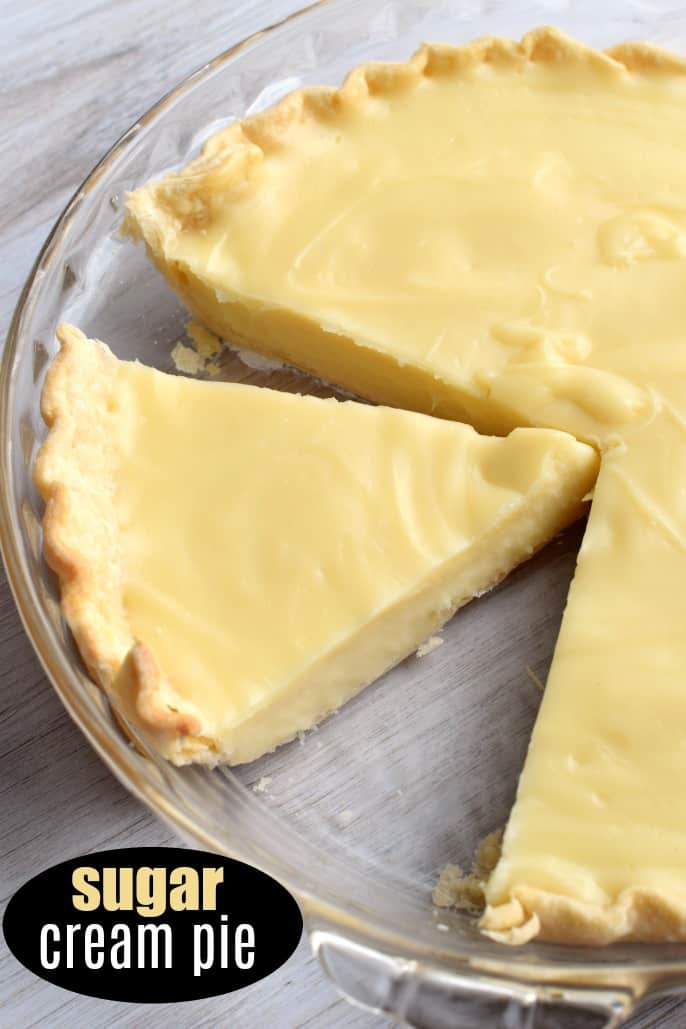 Sugar cream pie in a clear glass pie plate with one slice removed and another slice cut and ready to serve.