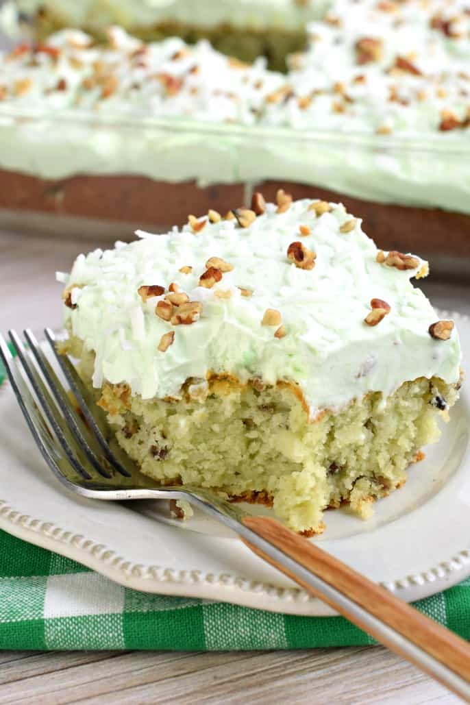 Slice of pistachio cake with pistachio frosting on a plate with a bite taken out.