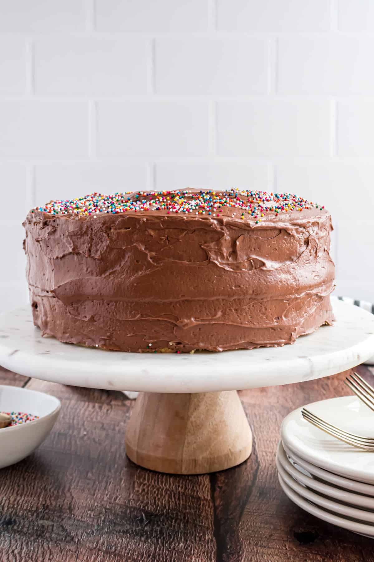 Yellow birthday cake with chocolate frosting and sprinkles on a white cake platter.