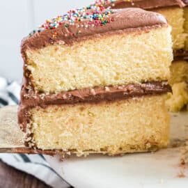 Two layers of yellow cake with chocolate frosting and sprinkles on a cake platter.