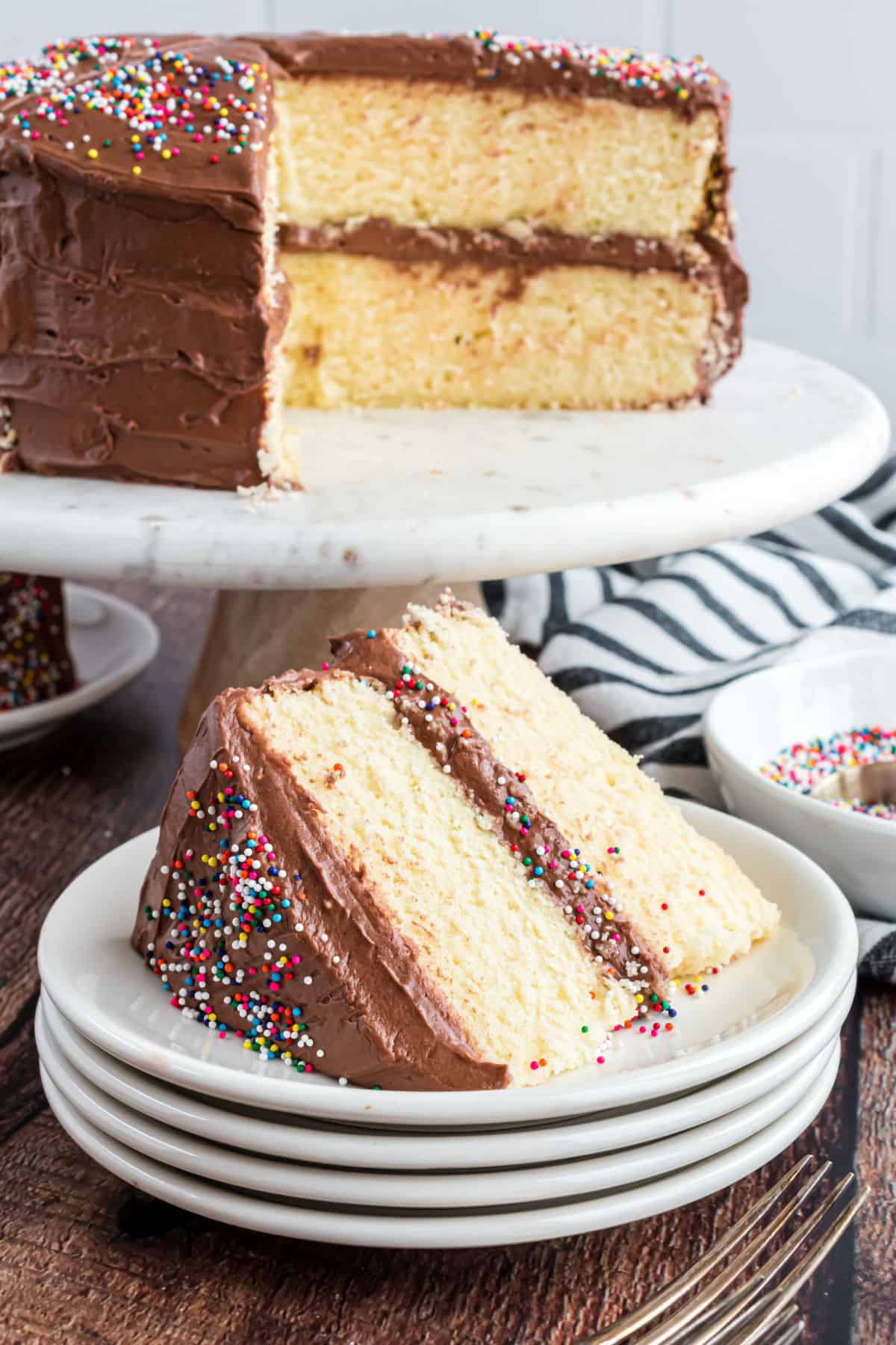 Slice of yellow layer cake on a stack of white plates.