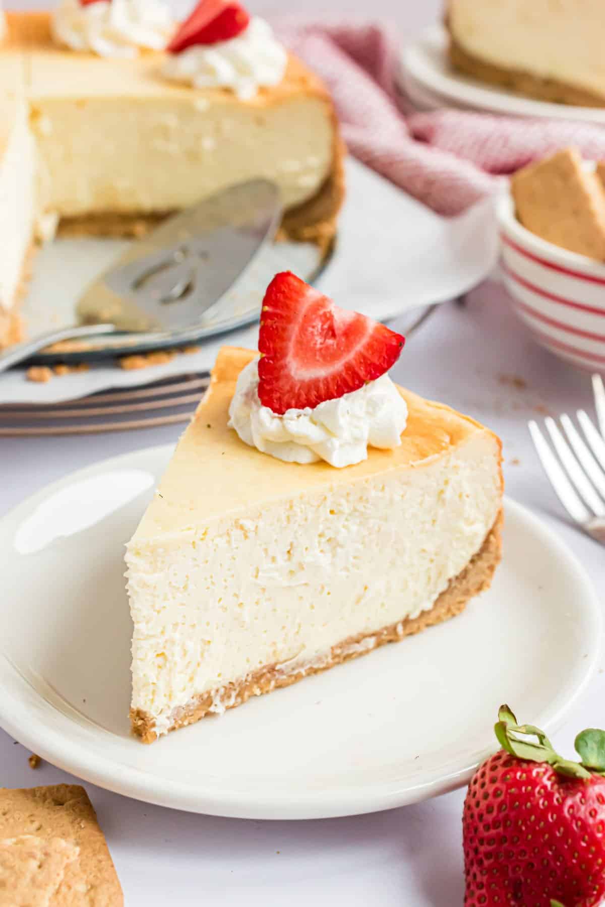 Slice of cheesecake with dollop of whipped cream and fresh strawberry on a white plate.