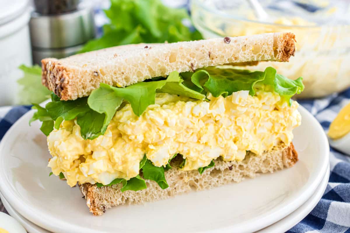 Half of an egg salad sandwich with lettuce on a white plate.