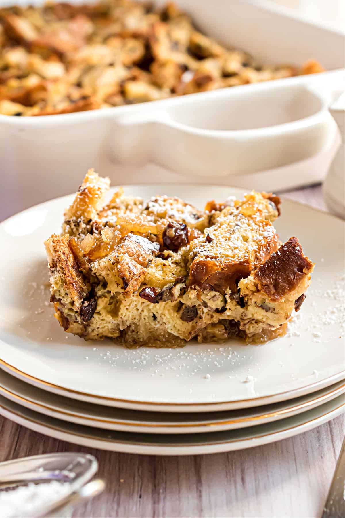 Slice of french toast casserole with powdered sugar on a stack of white plates.