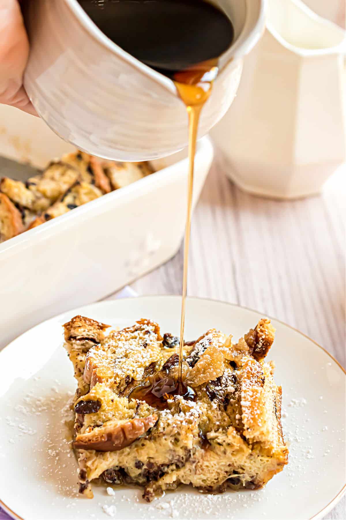 Syrup being poured over a slice of french toast casserole on a white plate.