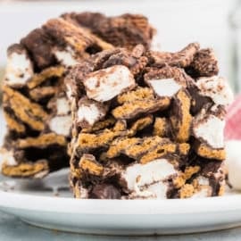 Close-up of two indoor s'mores bars with chocolate, marshmallows, and graham crackers stacked on a white plate.