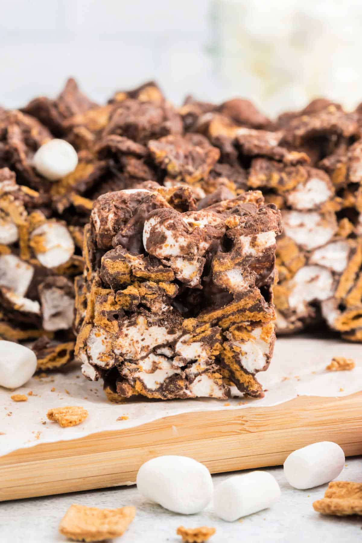 A close-up of indoor s'mores bars with layers of chocolate, marshmallows, and graham crackers on a wooden board.