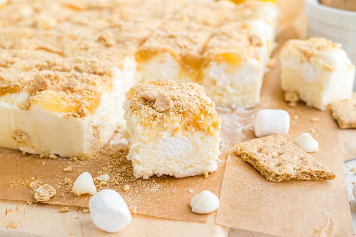 A close-up of lemon icebox dessert bars reminiscent of lemon meringue fudge, topped with graham cracker crumbs, marshmallows, and white chips.