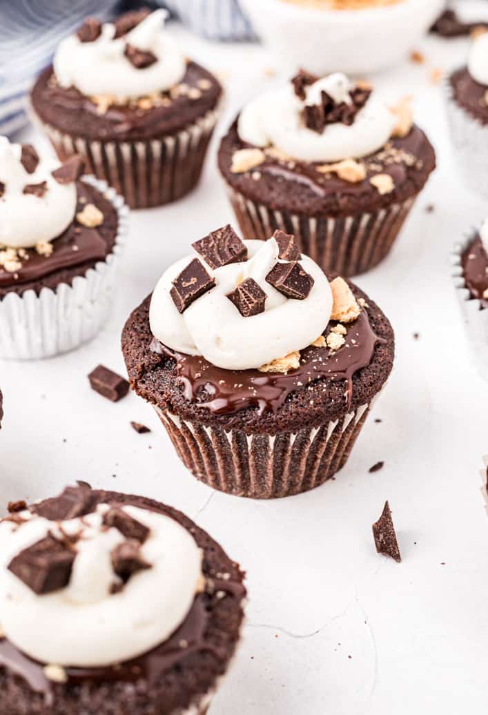 Chocolate smores cupcakes topped with ganache and frosting with chunks of graham cracker crumbs.