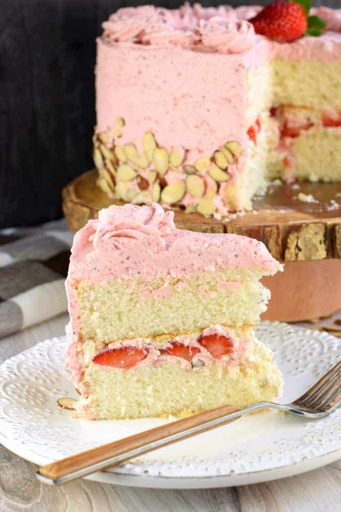 Slice of double layer almond cake with fresh strawberry frosting and berry filling on white plate.
