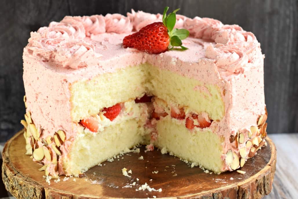 Strawberry Layer cake with big slice removed. On a wooden cake plate.