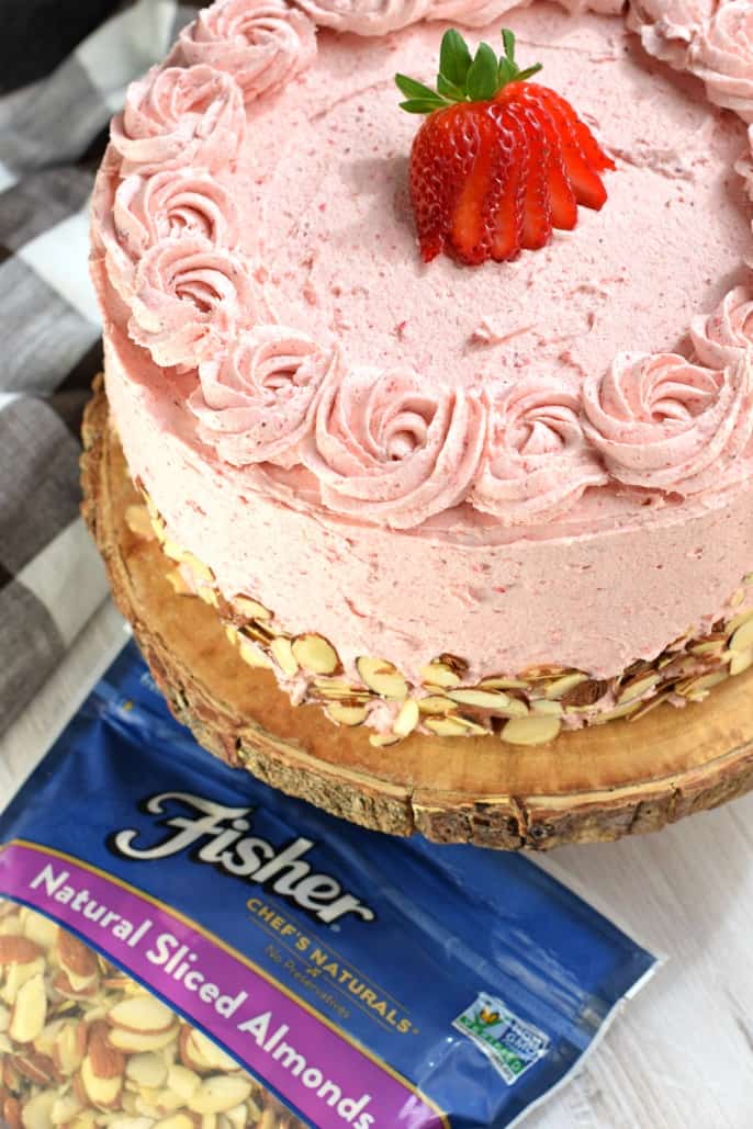 Strawberry Almond Cake on a wooden cake stand with a bag of Fisher Nuts Almonds.