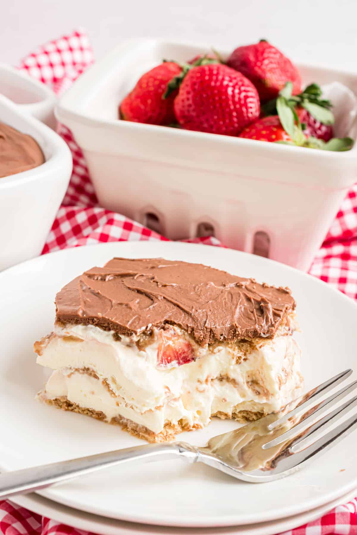 Slice of strawberry eclair cake on white plate with a bite taken.