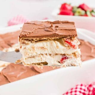 Slice of a layered strawberry eclair cake being lifted out of baking dish.