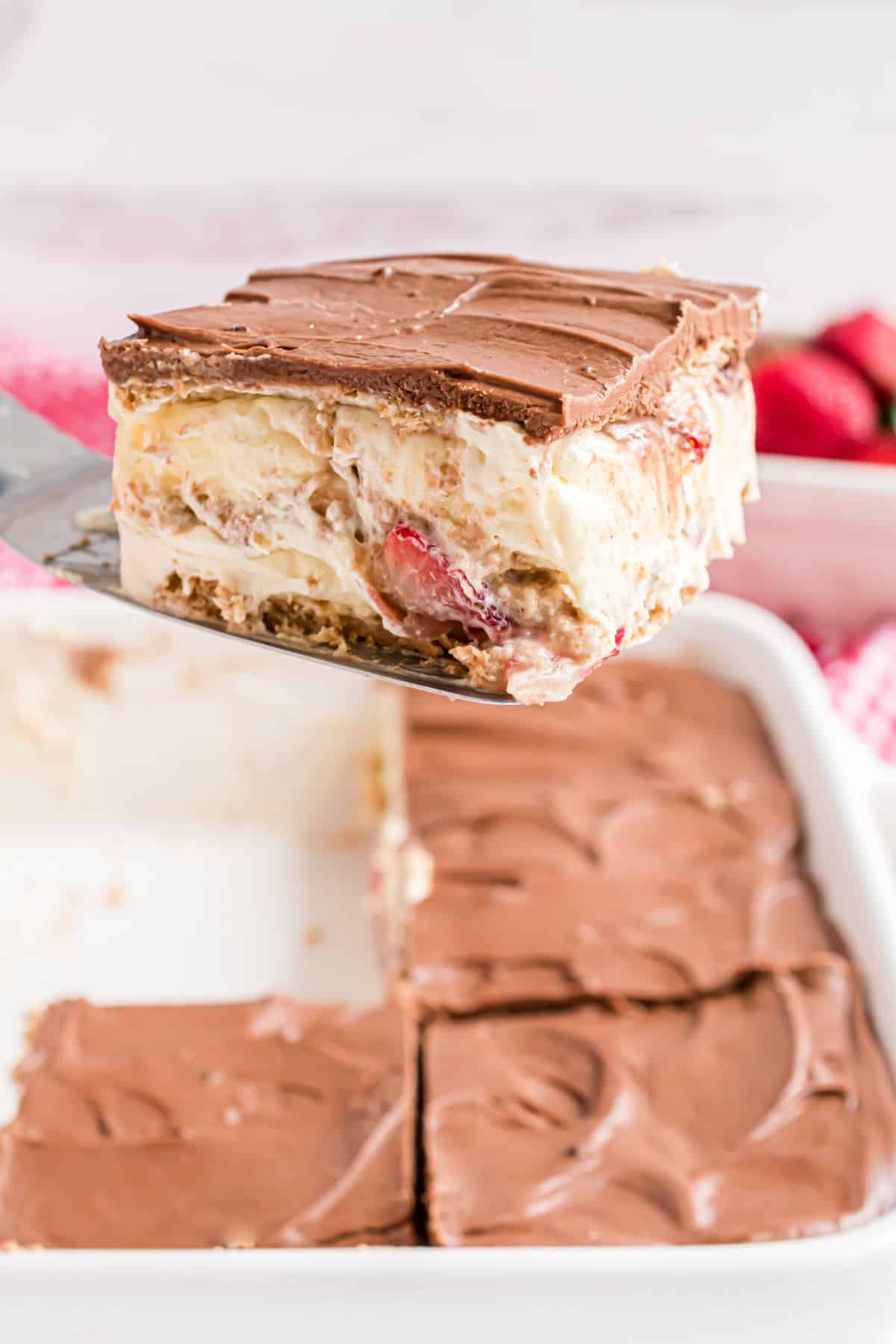 Eclair cake with strawberries being lifted out of a pan.