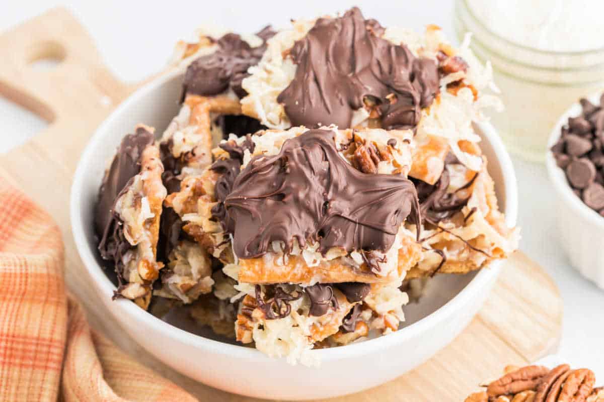 A bowl of pretzel bark topped with caramel, coconut, pecans, and melted chocolate on a wooden board.