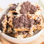 A bowl filled with caramel coconut cracker toffee, nut, and chocolate-topped dessert bars arranged in a stack.