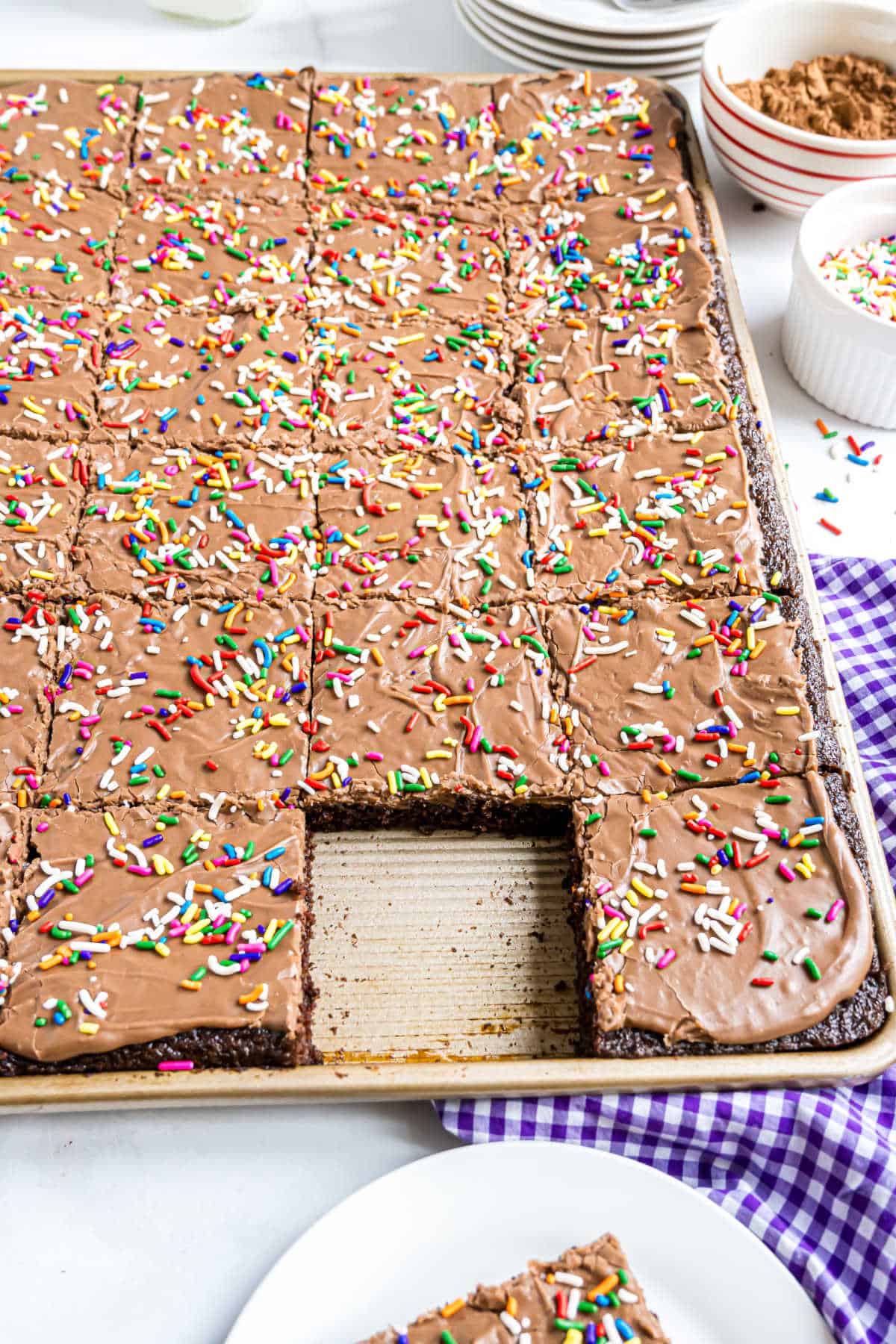 A chocolate buttermilk sheet cake with rich chocolate icing and rainbow sprinkles, one row cut out and removed.