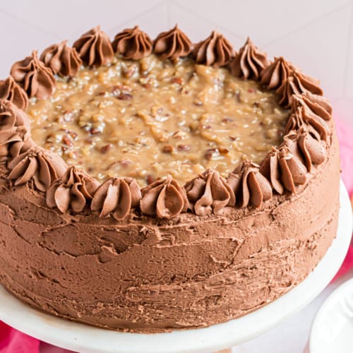 This German Chocolate Cake recipe, from scratch, is decadent and sweet with the rich chocolate cake layers topped with coconut pecan frosting! Add some chocolate buttercream frosting to put this cake recipe over the top!