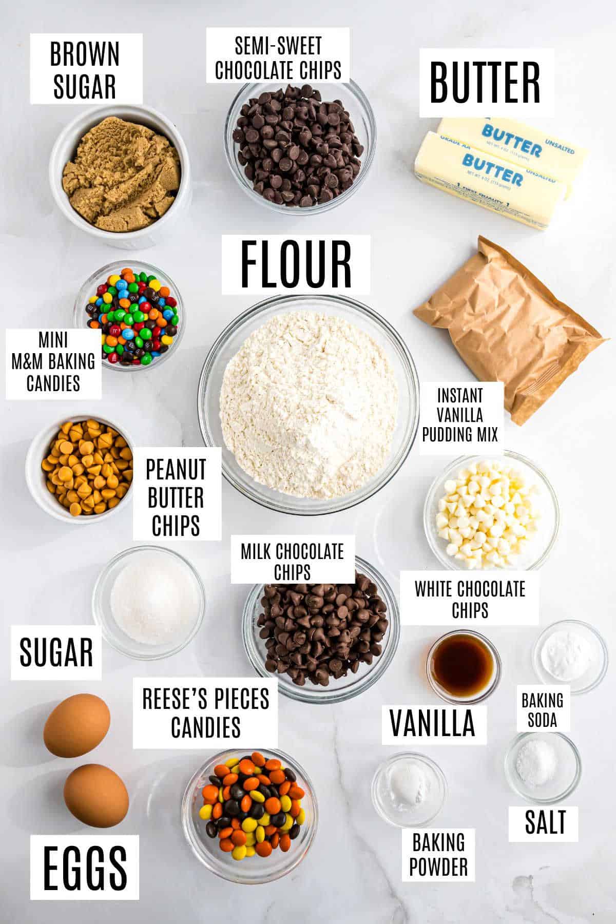 Assorted baking ingredients in bowls and cups labeled, including flour, sugar, butter, eggs, chocolate chips, and a special touch for pudding cookies.