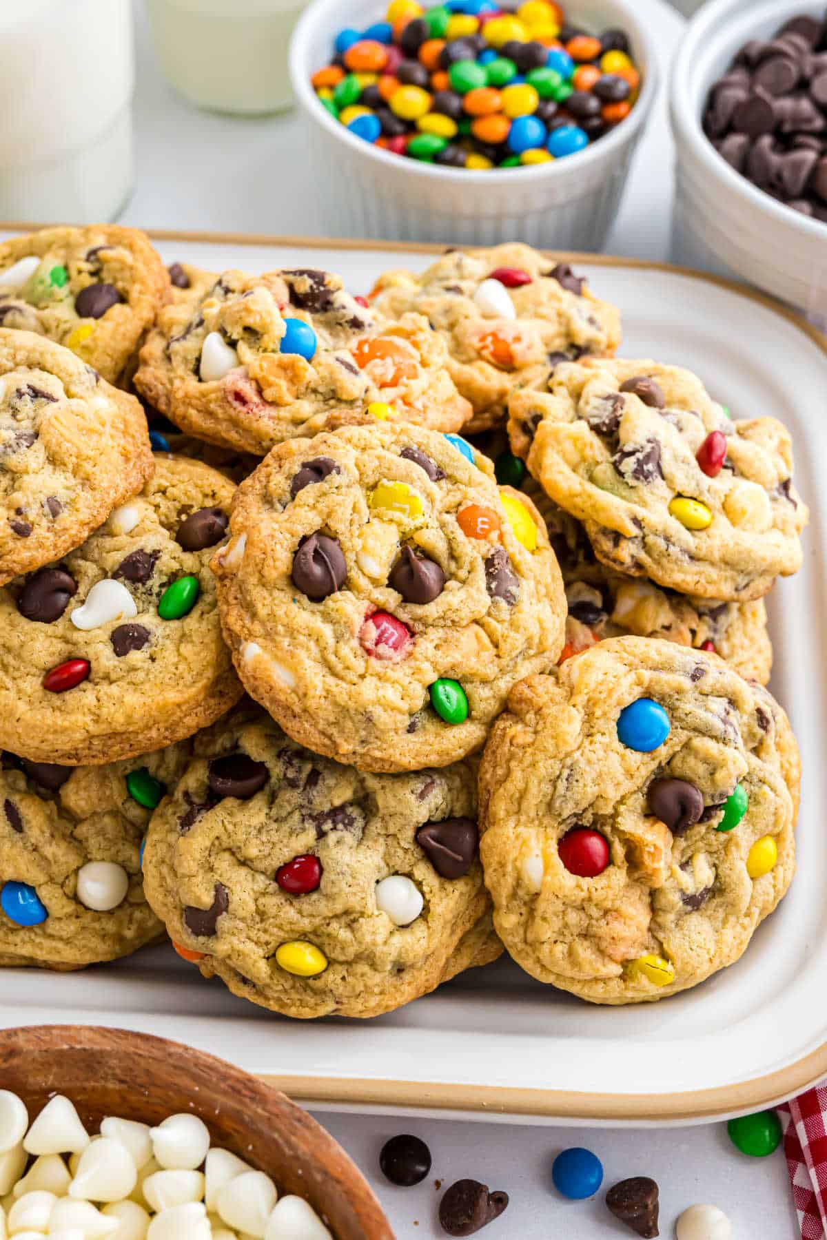 A plate of pudding cookies with chocolate chips and colorful candy-coated chocolates, surrounded by candy bowls.