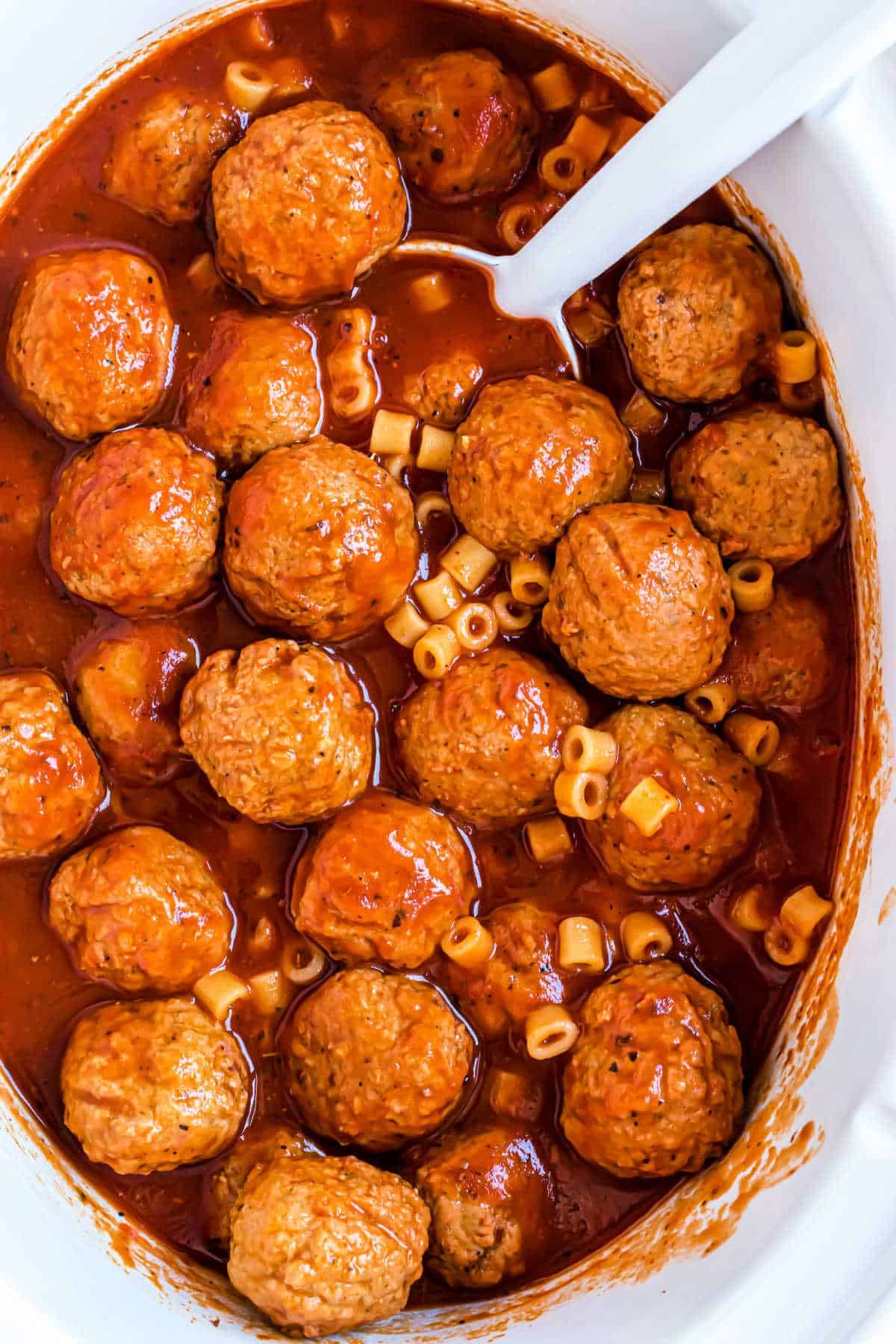 Spaghettios and meatballs in a white slow cooker.