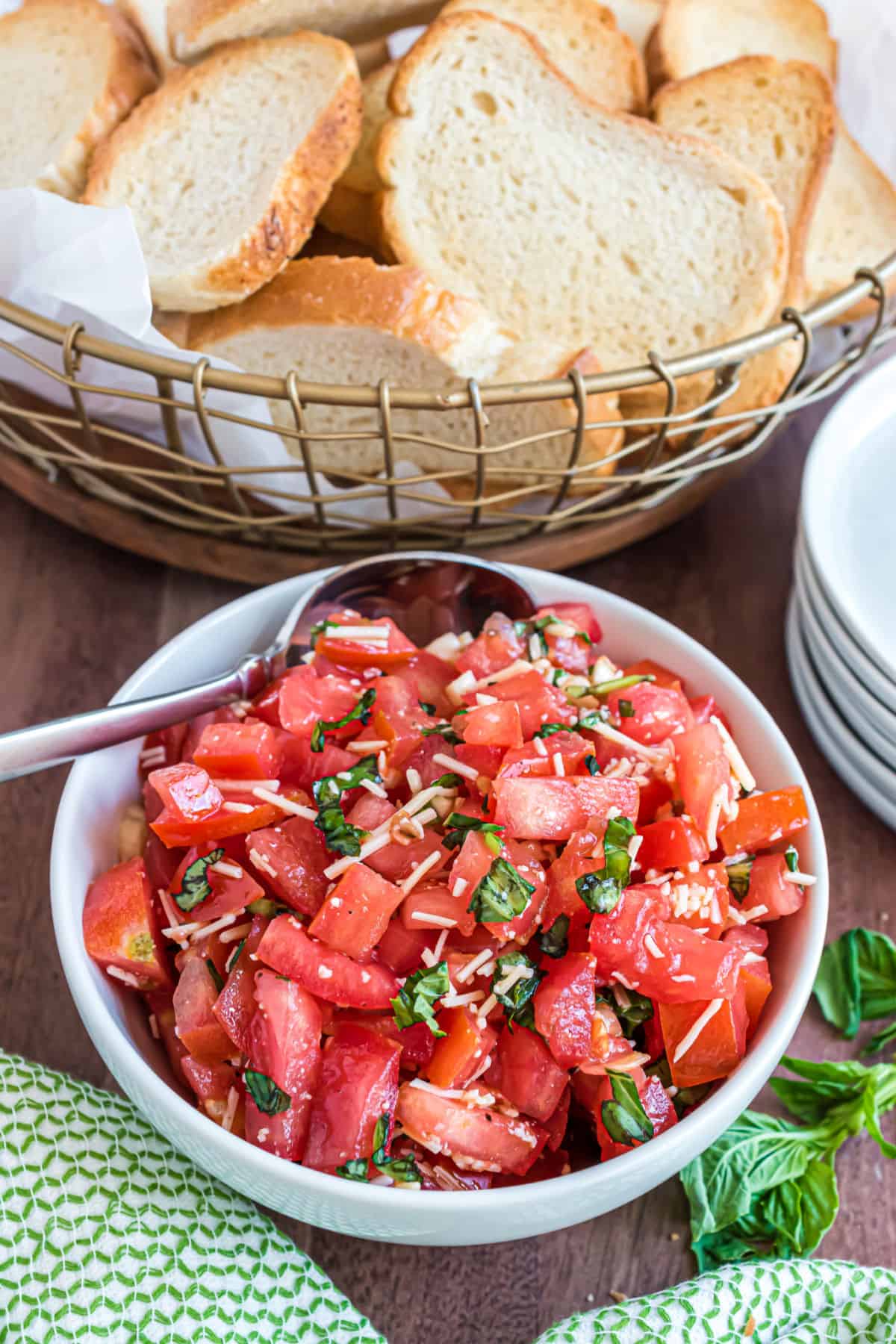 Bruschetta in a white bowl with toasted bread in wire basket.