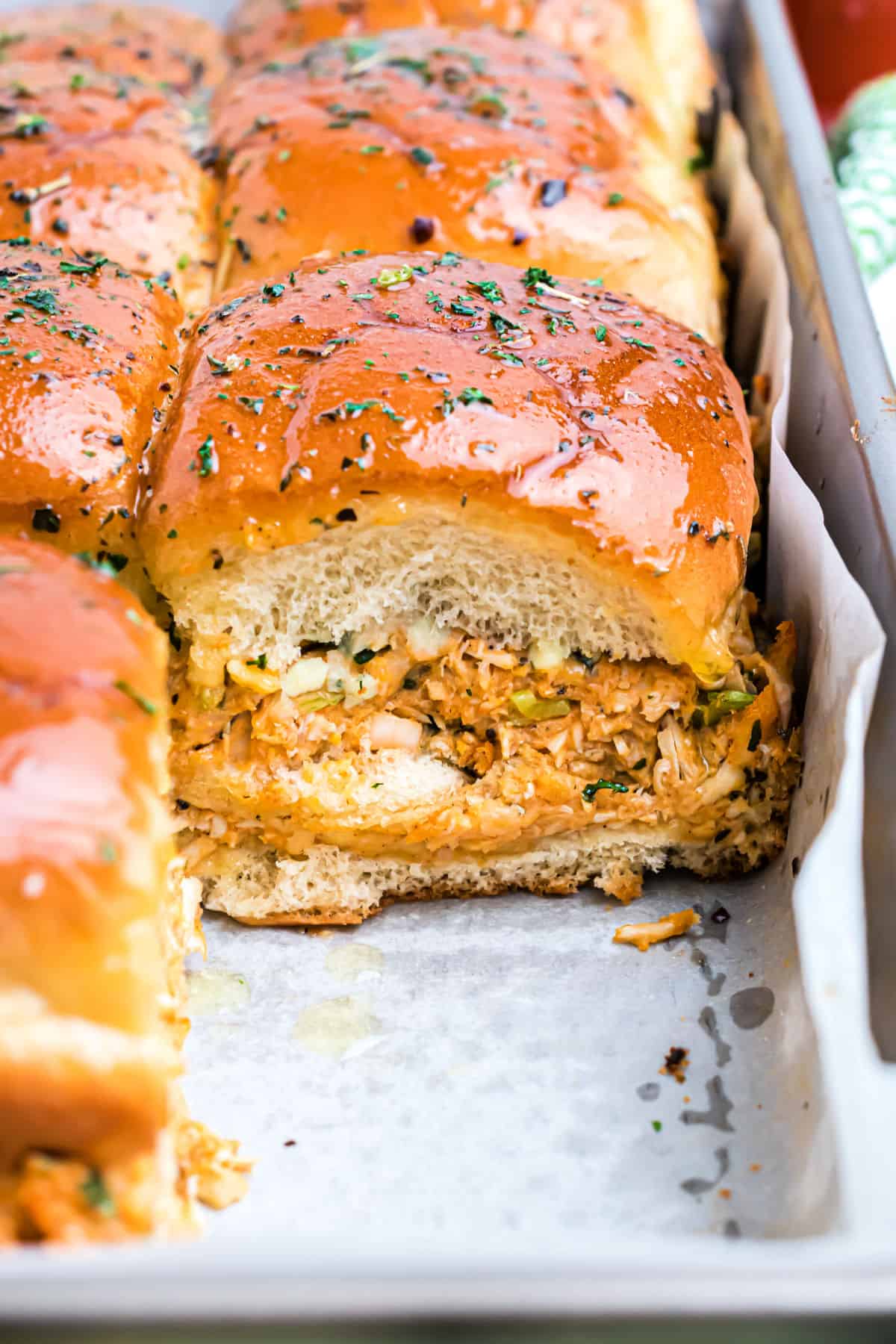 Hawaiian roll filled with buffalo chicken on a parchment paper lined baking sheet.