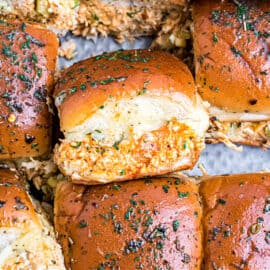 Buffalo chicken sliders stacked on a cookie sheet.