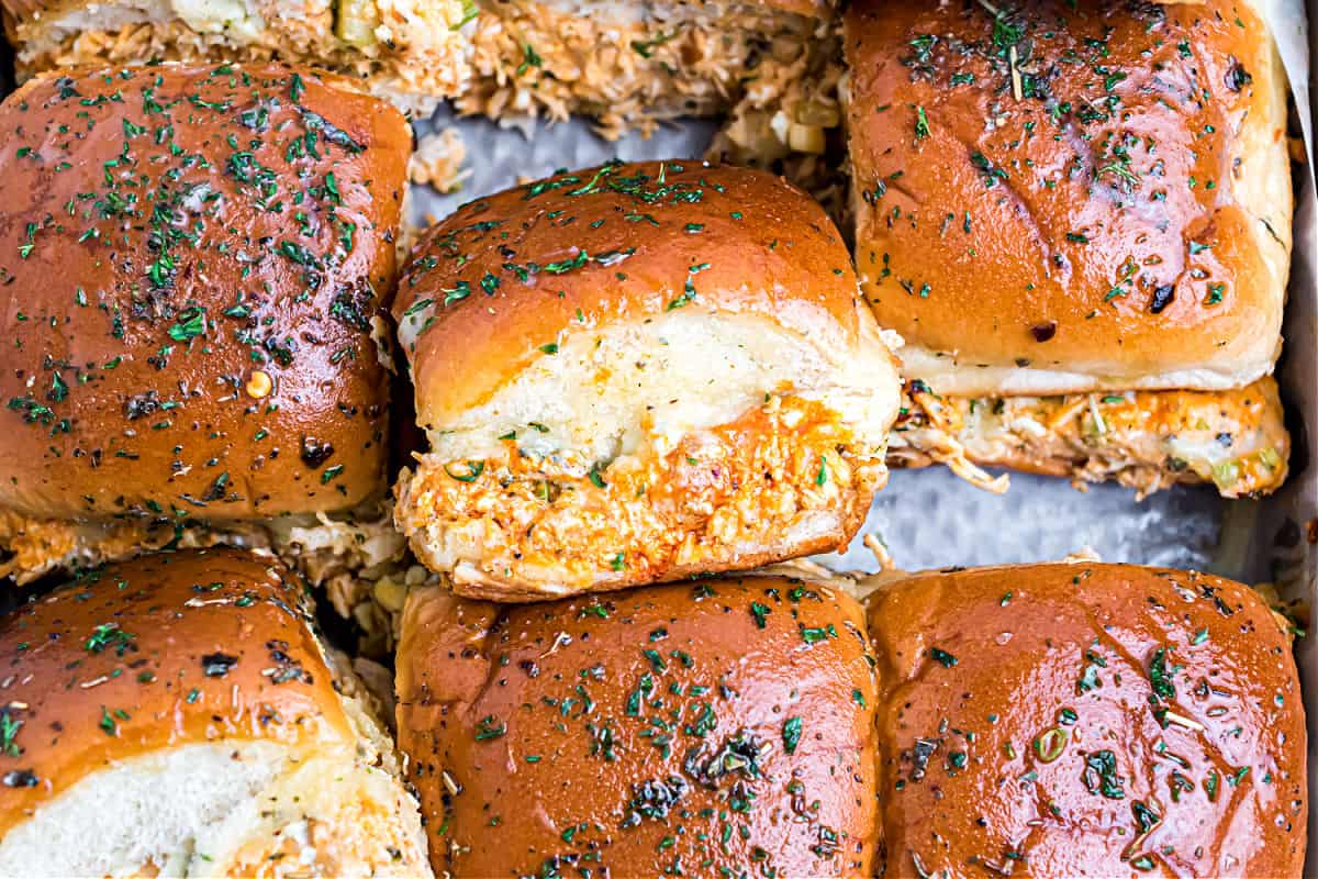 Buffalo chicken sliders stacked on a cookie sheet.