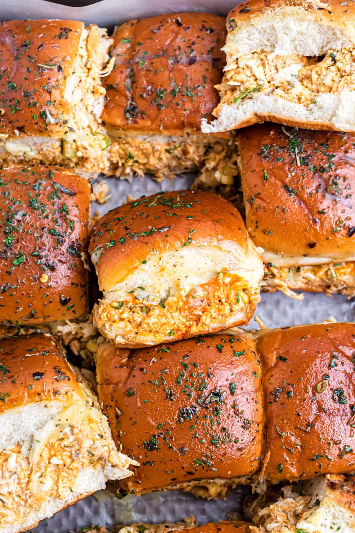 Buffalo chicken sliders stacked on a baking sheet.