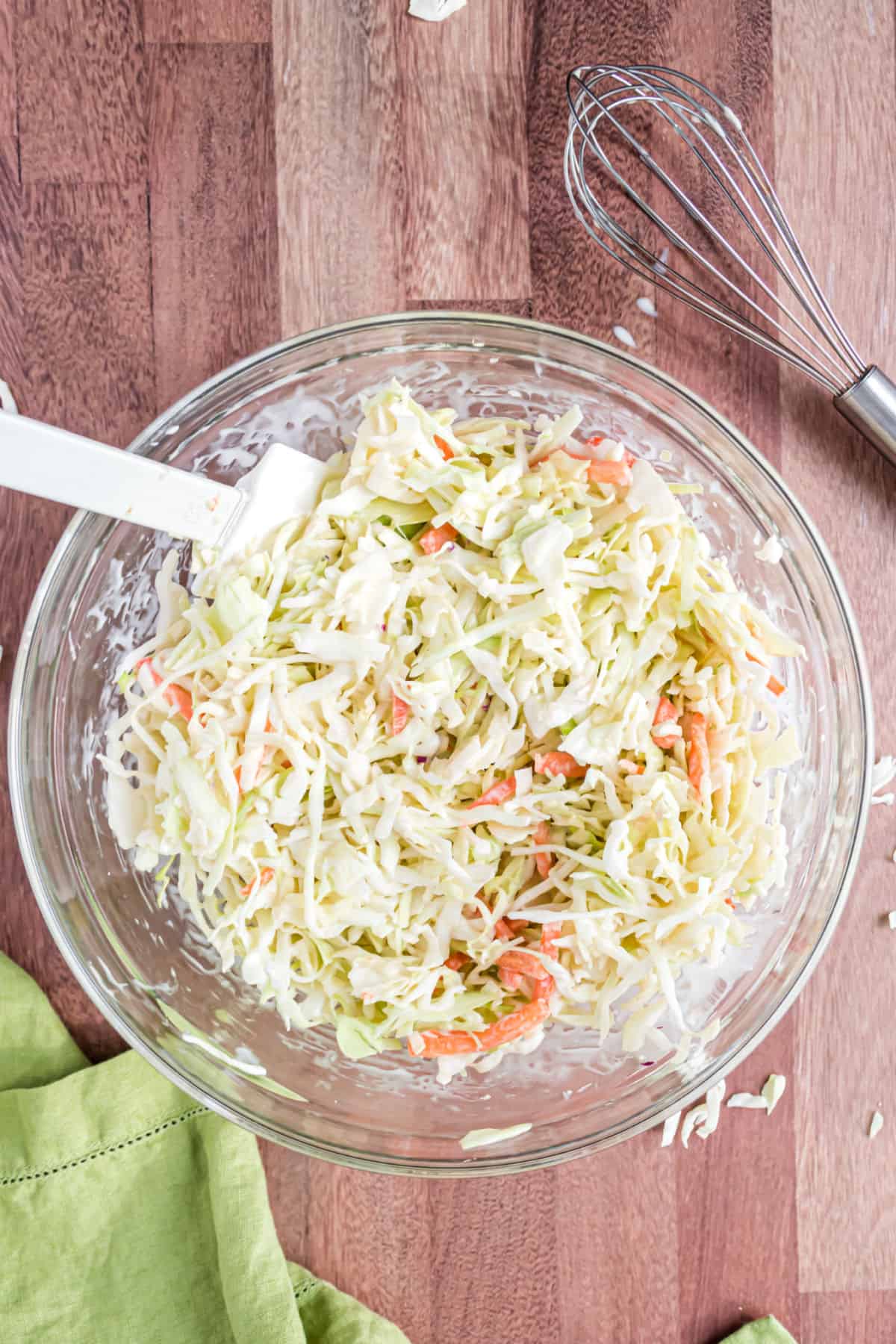 Creamy coleslaw in a clear glass bowl with white spatula.