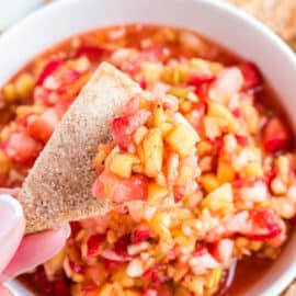 Fruit salsa in a white bowl being scooped with baked cinnamon tortilla chips.
