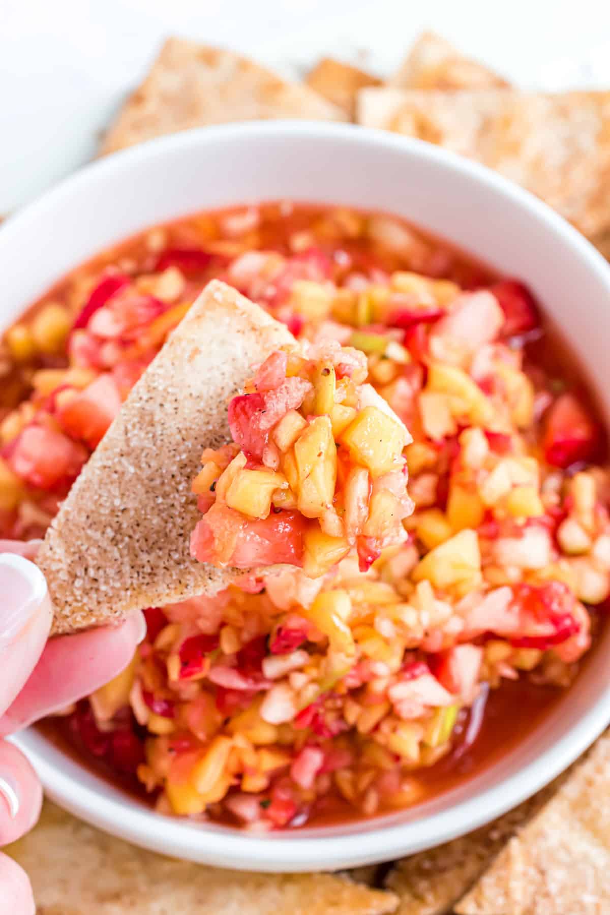 Fruit salsa in a white bowl being scooped with baked cinnamon tortilla chips.