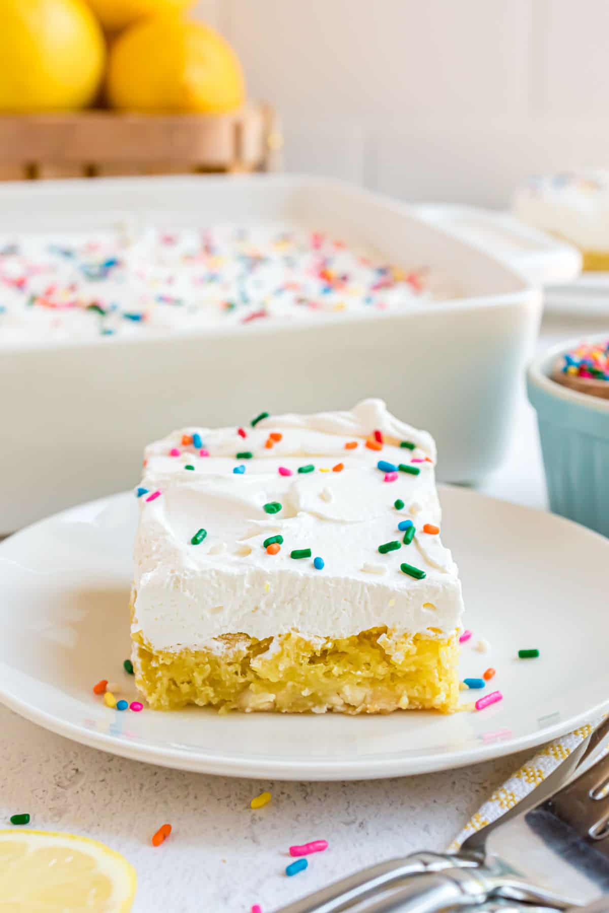 Slice of lemon cake with cool whip on a white plate.