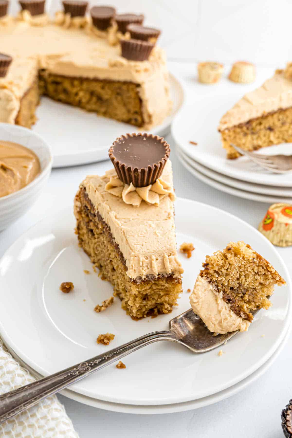 A slice of Reese's peanut butter cake with frosting and a peanut butter cup on top, served on a white plate.