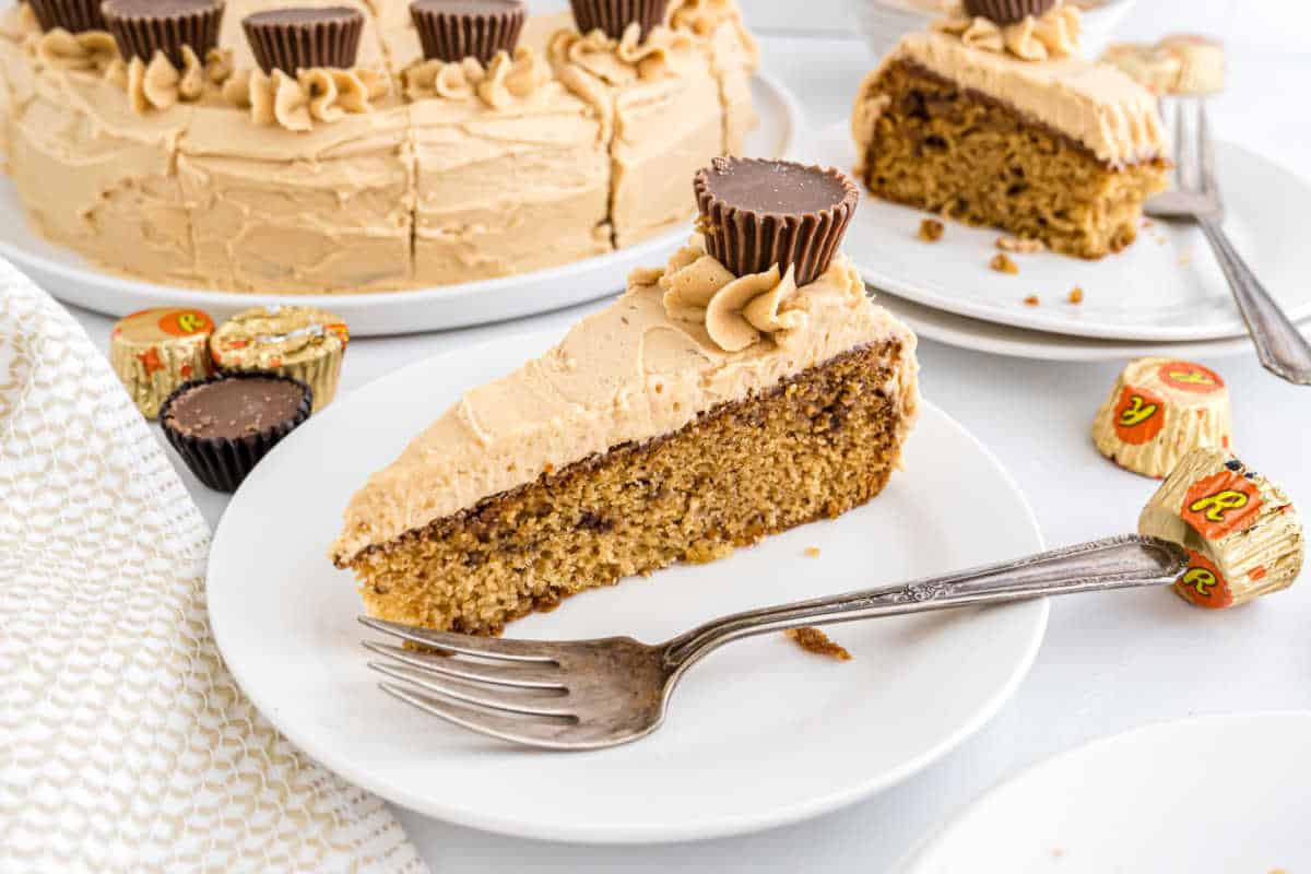 Slice of Reese's peanut butter cake with creamy peanut butter frosting and a mini peanut butter cup on a white plate with a fork.