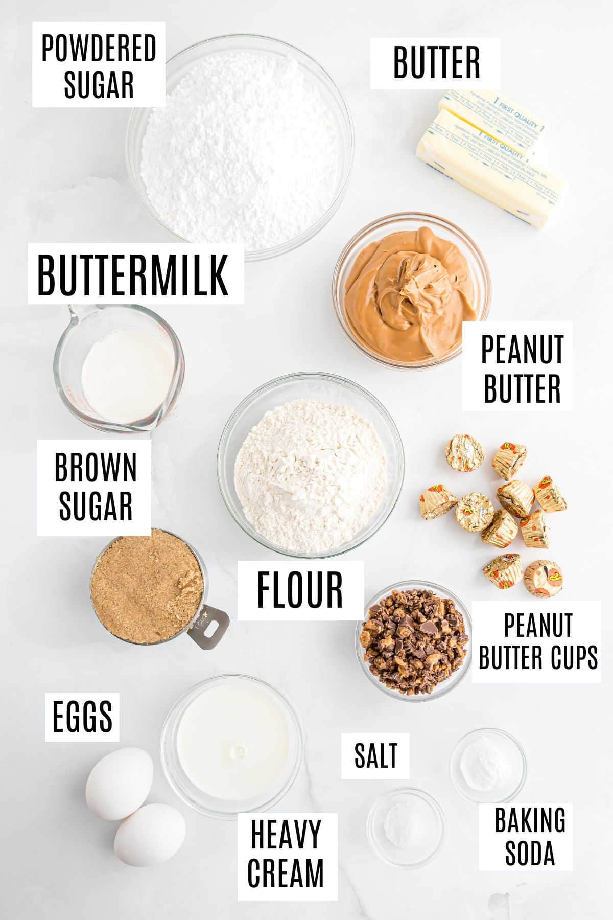 Overhead view of labeled baking ingredients for a Reese's peanut butter cake: flour, eggs, butter, buttermilk, sugars, peanut butter, cream, candy, salt.